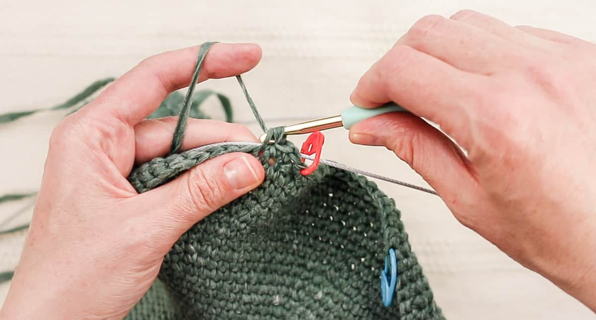 Hands crocheting a wire rope into the brim of a crochet hat.