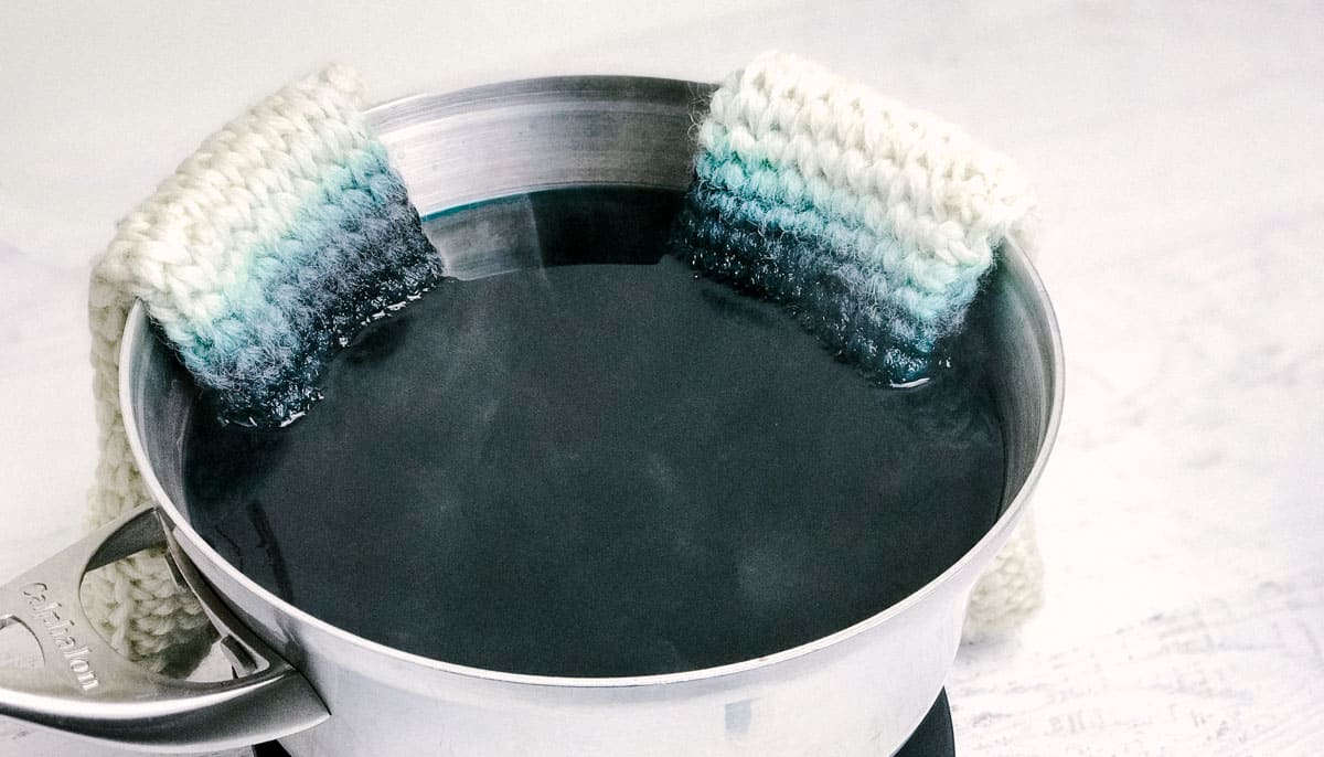 Yarn being dip dyed in a pot of blue food coloring.