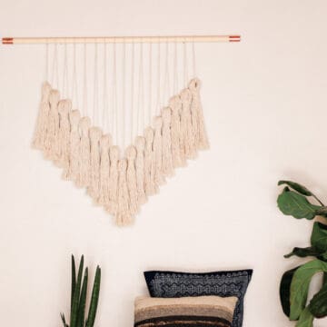 A beautiful DIY yarn wall hanging in a boho living room. The wall hanging uses copper pipe fittings to add a bit of glam.