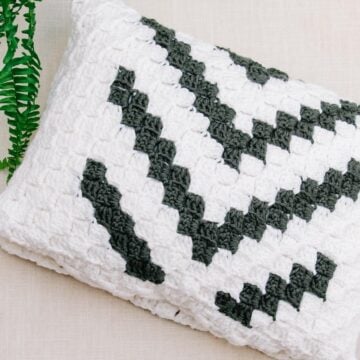 A graphic corner to corner crochet pillow made with off white and grey yarn.