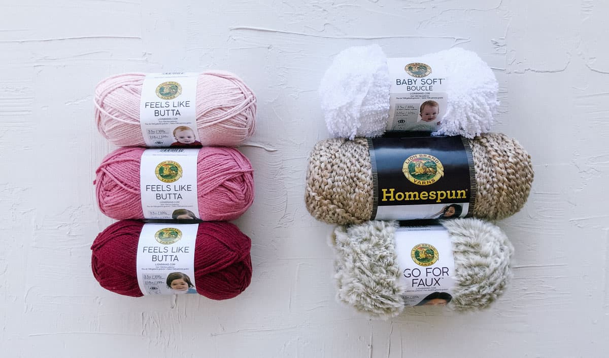 Six balls of Lion Brand yarn including Feels Like Butta, Homespun, Go for Faux and Baby Soft Boucle.