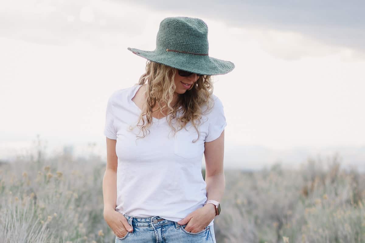 Woman standing in a field wearing a fedora crochet sun hat made with raffia-like yarn.