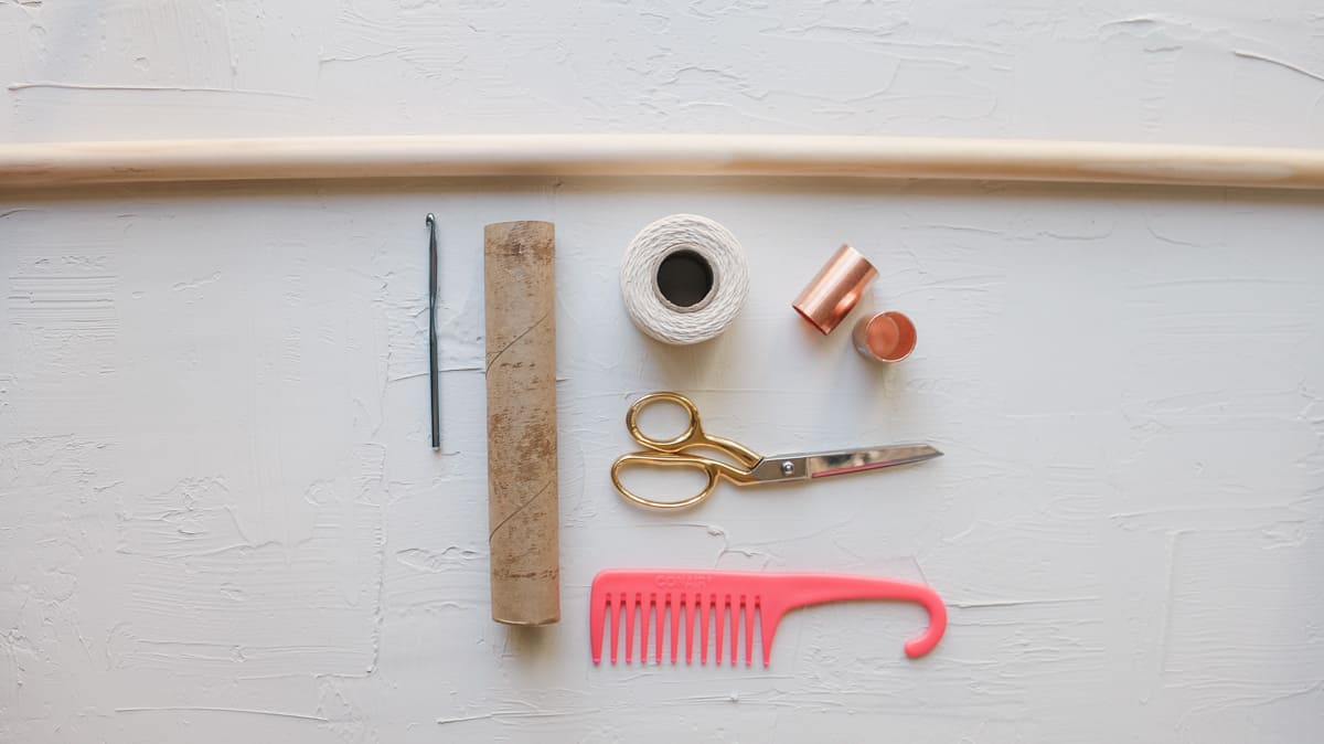 The supplies to make a yarn wall hanging including cotton twine, copper pipe fittings and a paper towel tube.