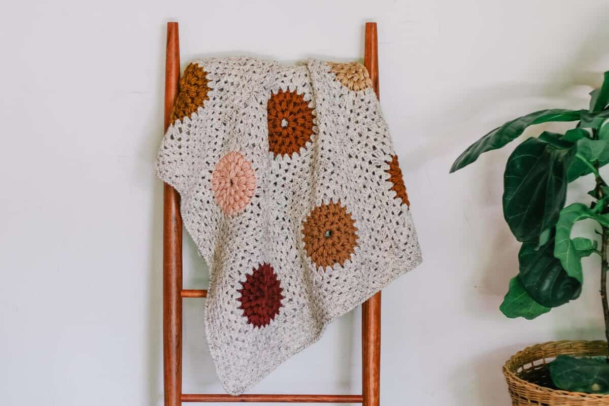 Crochet puff stitch granny square blanket hanging on a mid century blanket ladder.