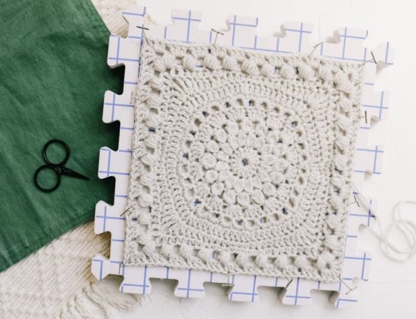 A crochet square made with bobble and puff stitches pinned to a foam blocking board.