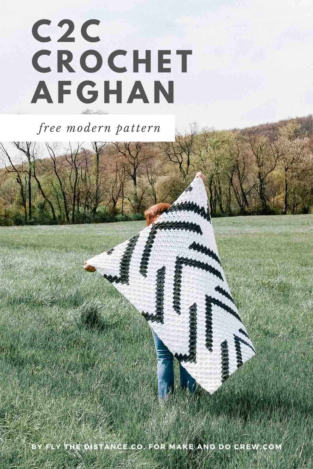 A woman in a field holding up a corner to corner crochet blanket with arrows on it.