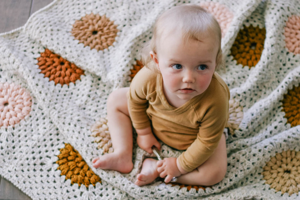 A baby sitting on a handmade crochet granny square baby blanket.
