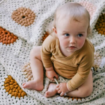 A baby sitting on a handmade crochet granny square baby blanket.