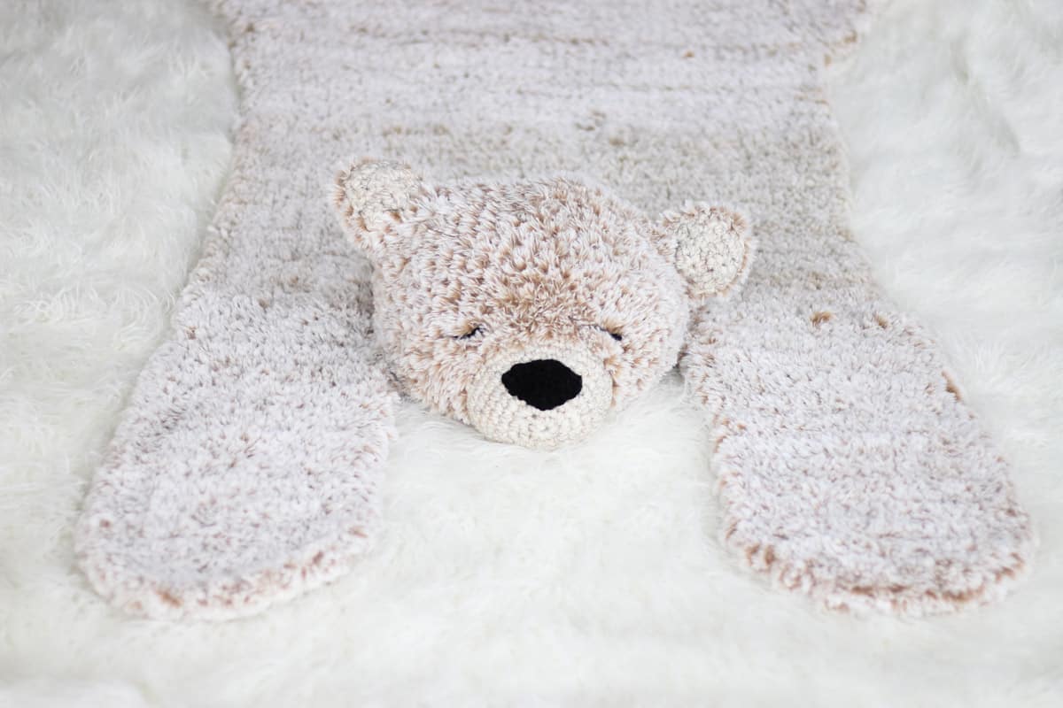 A crocheted faux fur bear blanket rug laying on a white floor.
