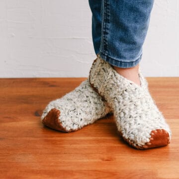 An adult woman wearing an easy pair of crochet slippers made from rectangles. Each slipper has a leather sole.