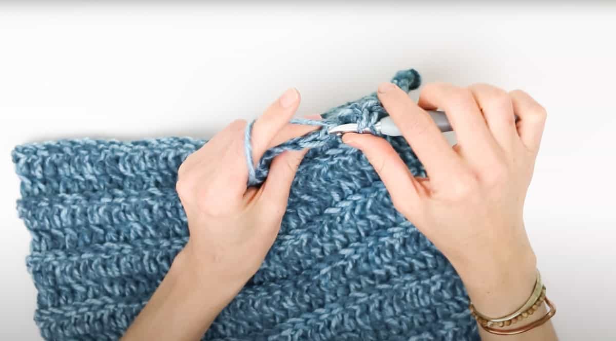 An overhead shot showing how to seam the rectangle using a crochet hook on a white background.