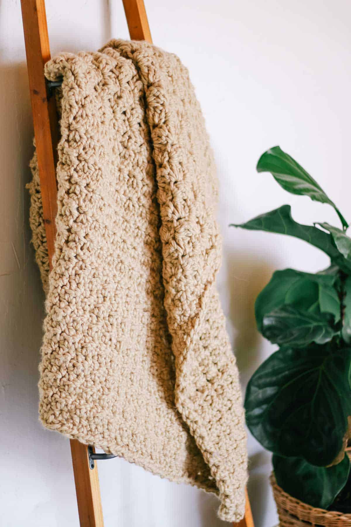 A tan-colored chunky crochet blanket draped on a blanket ladder.