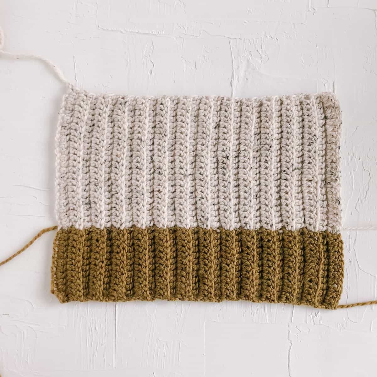 A color blocked crochet rectangle that is green on the bottom half and cream colored on the top section.