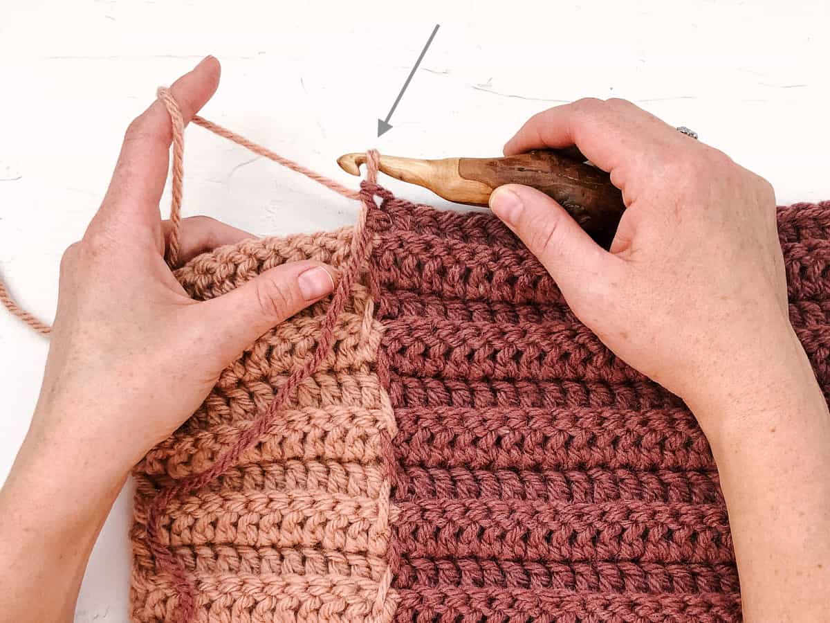 Two hands holding a crochet hook and pink yarn demonstrating how to change colors in the middle of a row of crocheting.