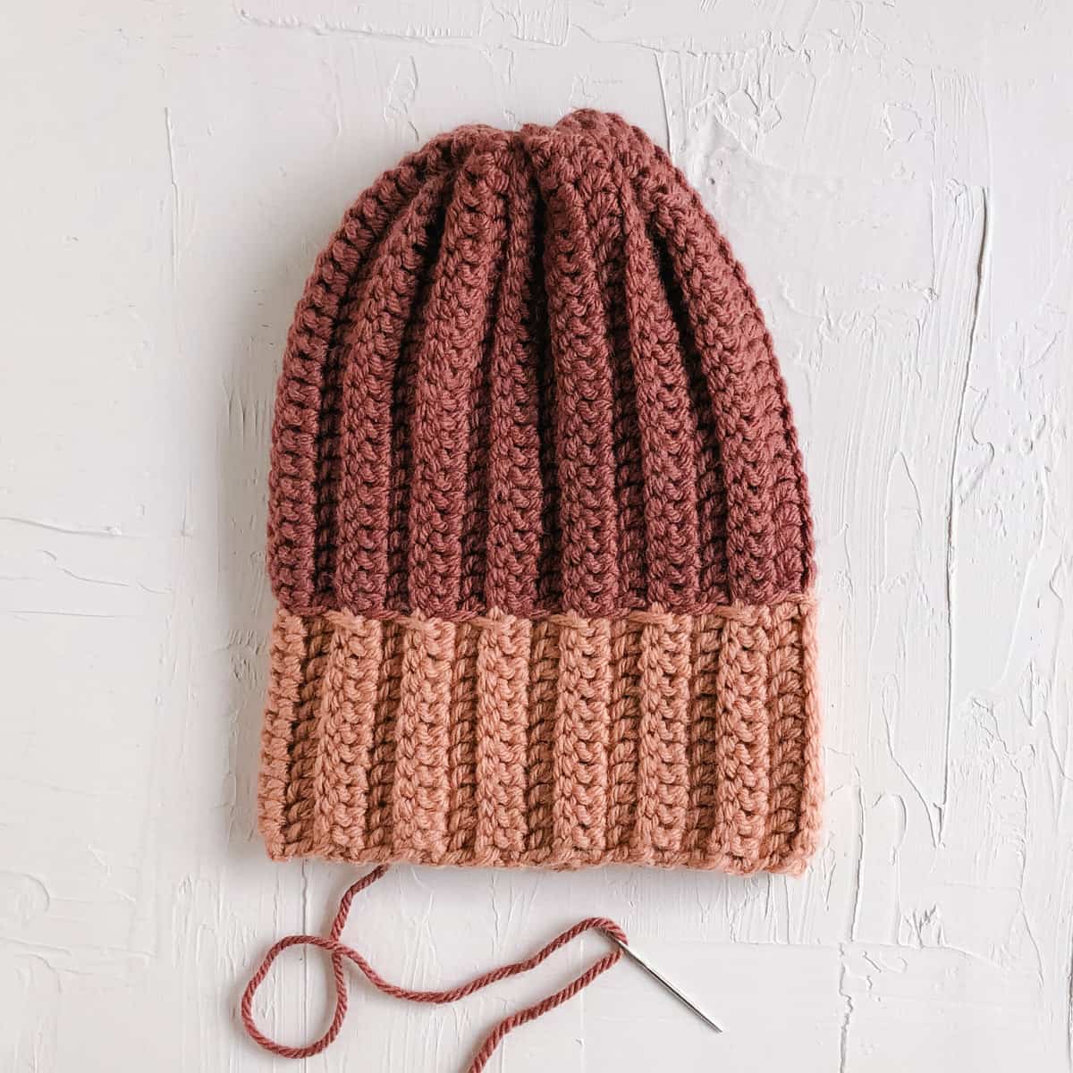 A ribbed pink crochet hat in progress. The top is cinched closed to create the top of the beanie.