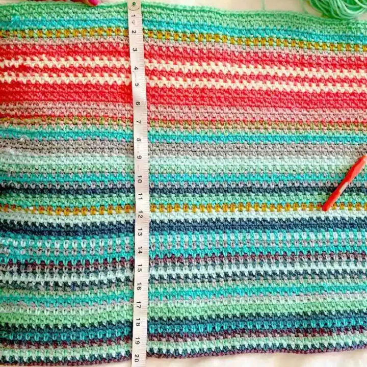 A temperature blanket is measured using a tape measure with a hook and yarn skein.