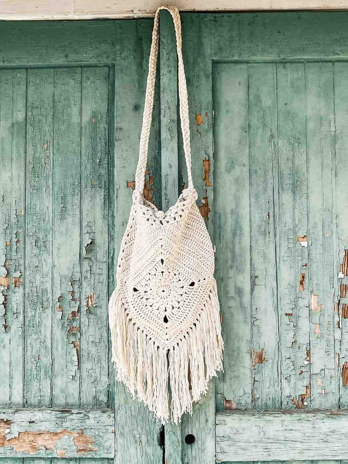 Crocheted boho bag with long fringe hanging on a rustic wall.