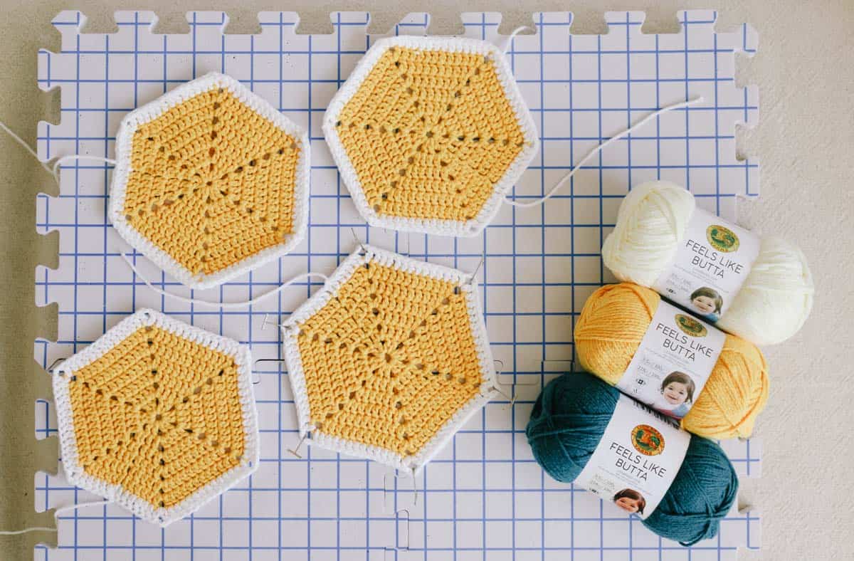Yellow crochet hexagons pinned to a blocking board sitting next to Lion Brand Feels Like Butta.