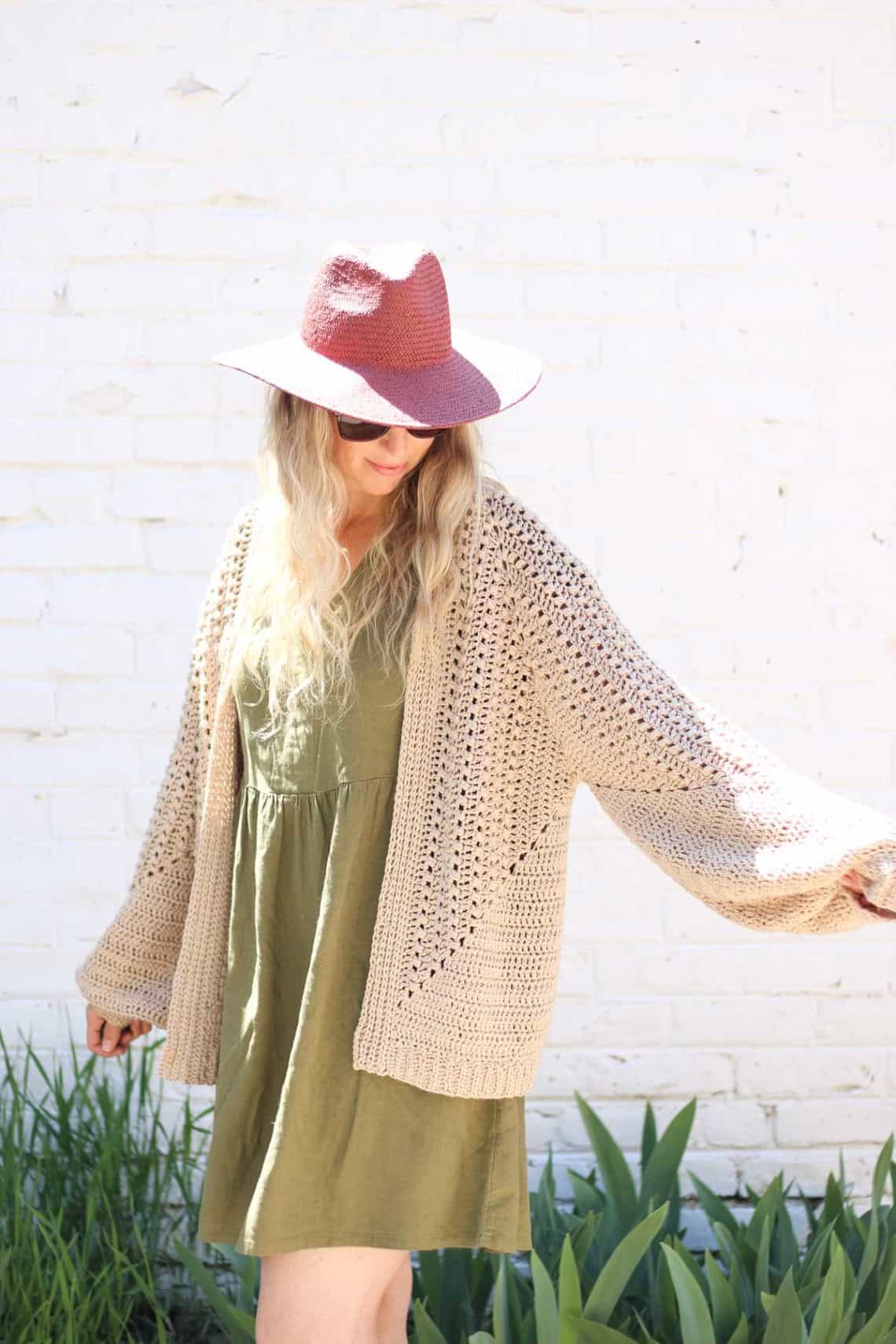 A blonde woman wearing a floral dress and a crochet hexagon cardigan made with Lion Brand Coboo in the color "Mauve."