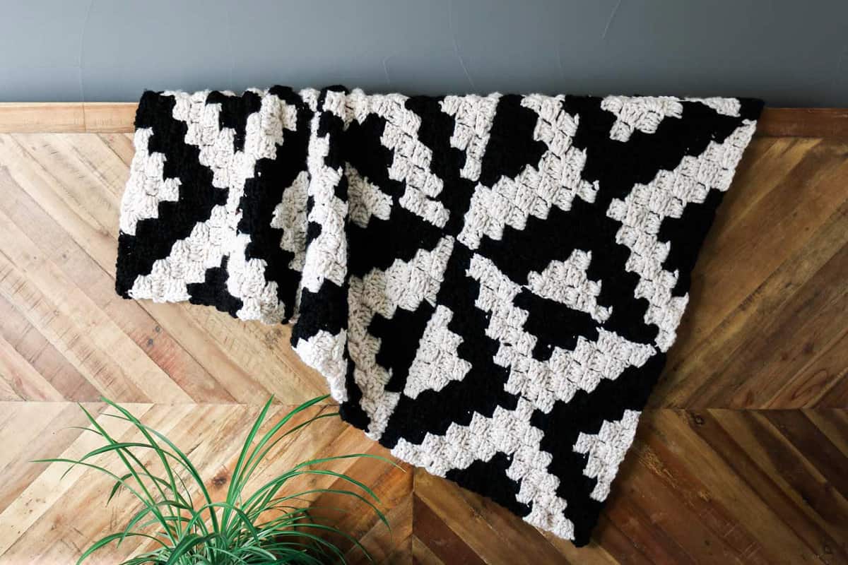 A graphic, modern corner to corner crochet blanket draped over a wooden ledge.