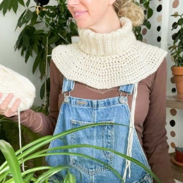 Woman wearing a partially complete crochet sweater worked from the top down. She is holding a ball of Lion Brand Heartland yarn.