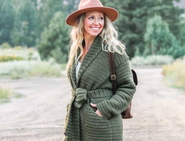 A woman on a dirt road in the mountains wearing a crochet sweater jacket made with Lion Brand Touch of Alpaca yarn in the color "Olive You."
