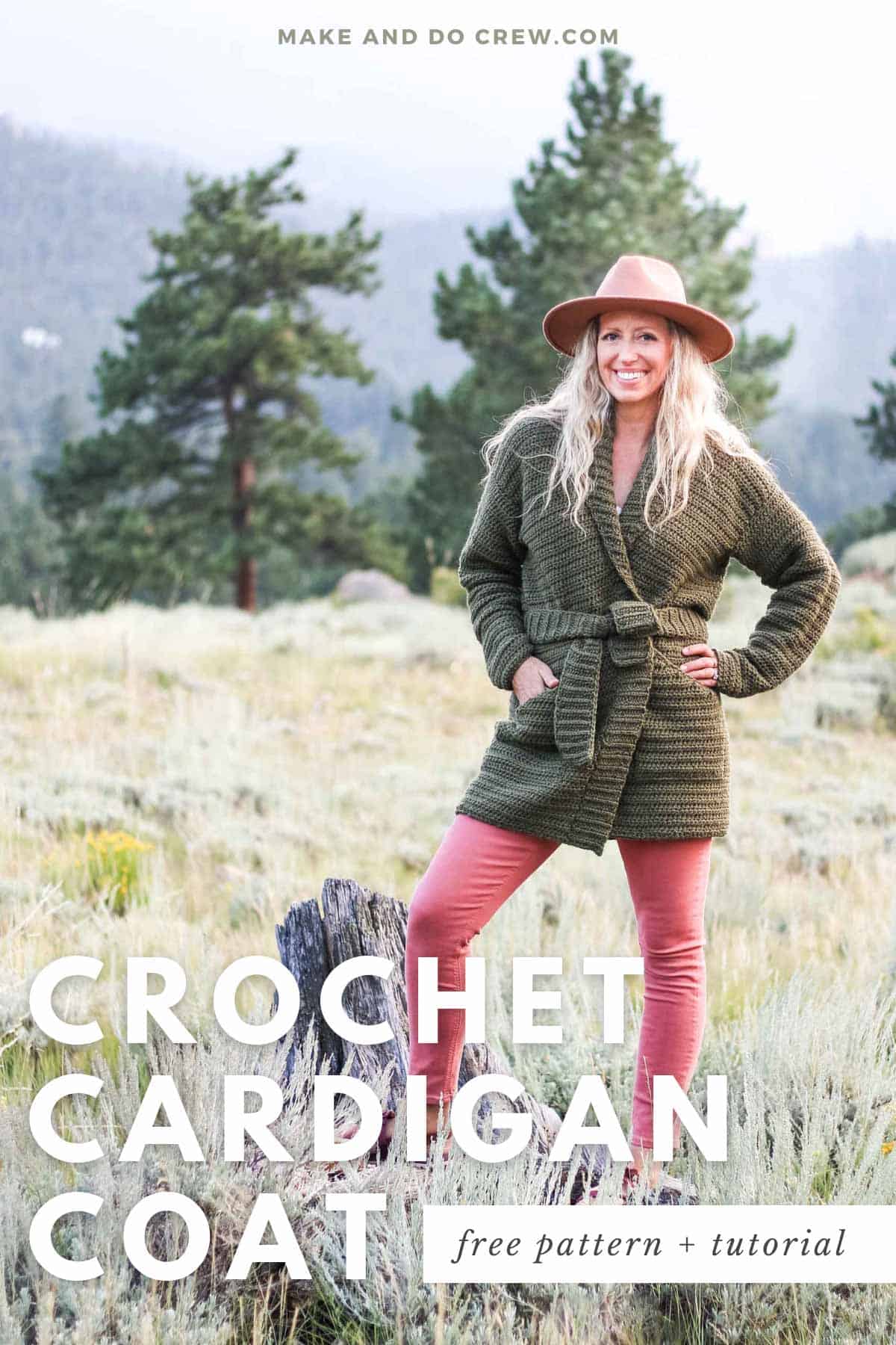 A woman smiling while wearing an olive green backpacker-free crochet cardigan coat with pockets, a belt, and a fedora hat.