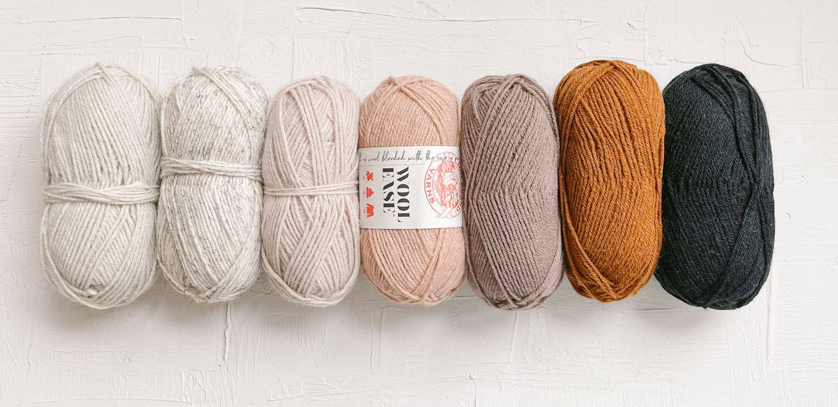 A row of Lion Brand Scarfie yarn in neutral colors, a brown color and a dark gray color. 