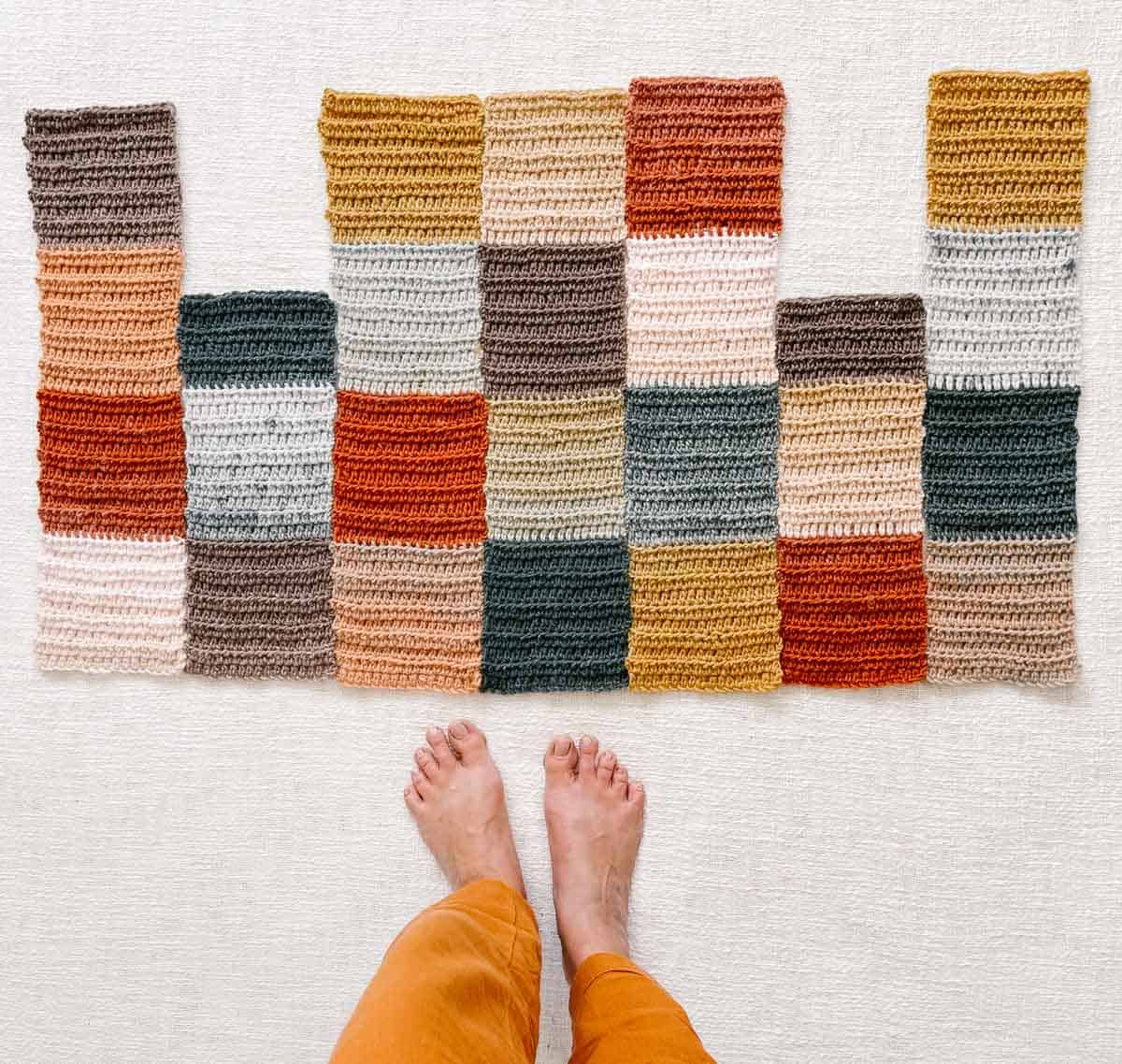 An overhead view of a colorful in-progress crochet patchwork sweater and a caucasian women's feet.