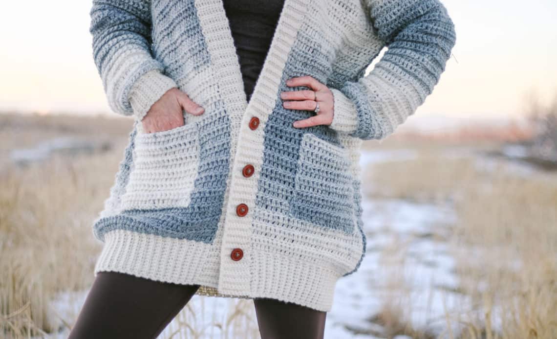 A close up of a crochet sweater made with Lion Brand Scarfie yarn. The sweater is buttoned down the front and the woman wearing it has her hands in her pockets.