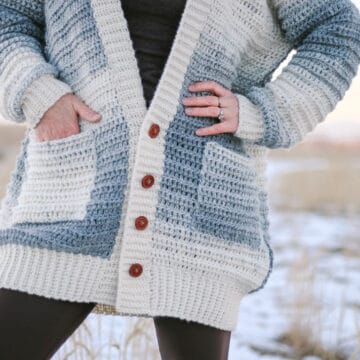 A close up of a crochet sweater made with Lion Brand Scarfie yarn. The sweater is buttoned down the front and the woman wearing it has her hands in her pockets.
