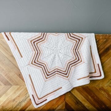 A crochet 8 point star blanket draped over a wooden bed.