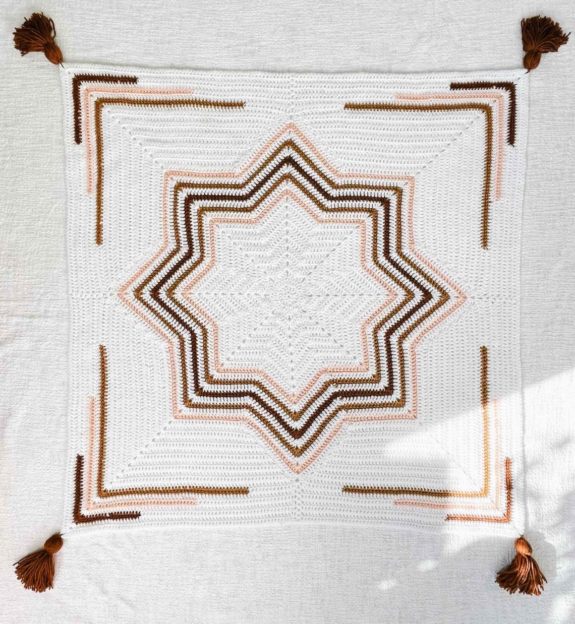 A crochet star baby blanket that has been squared off laying flat on the floor.