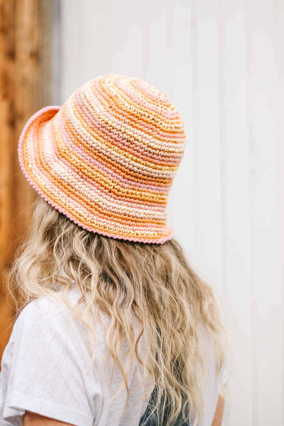 This image shows a woman with blond hair wearing a pink and orange crochet bucket hat. This image shows the back of the crochet bucket hat.