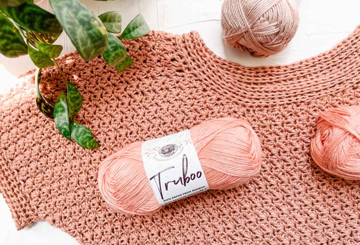 A skein of Lion Brand Truboo laying on top of a crocheted tunic made from the same yarn.