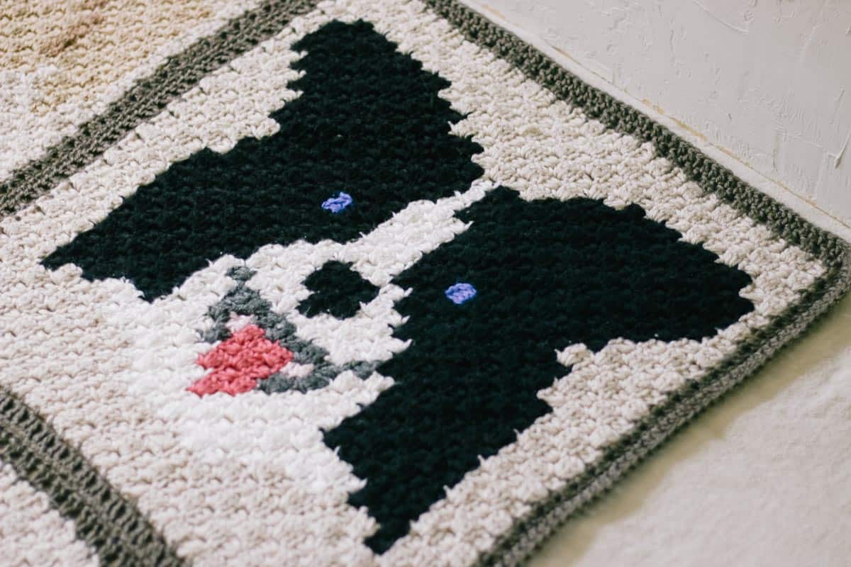 An overhead image of a c2c crochet border collie with a pink tongue.