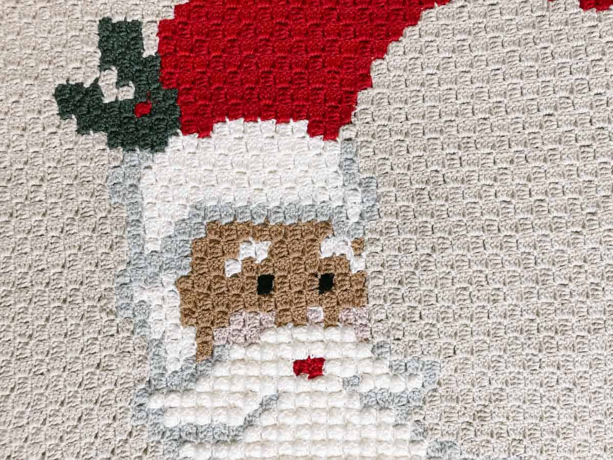This image shows a close up photo of a Santa face, as part of a corner to corner crochet blanket.