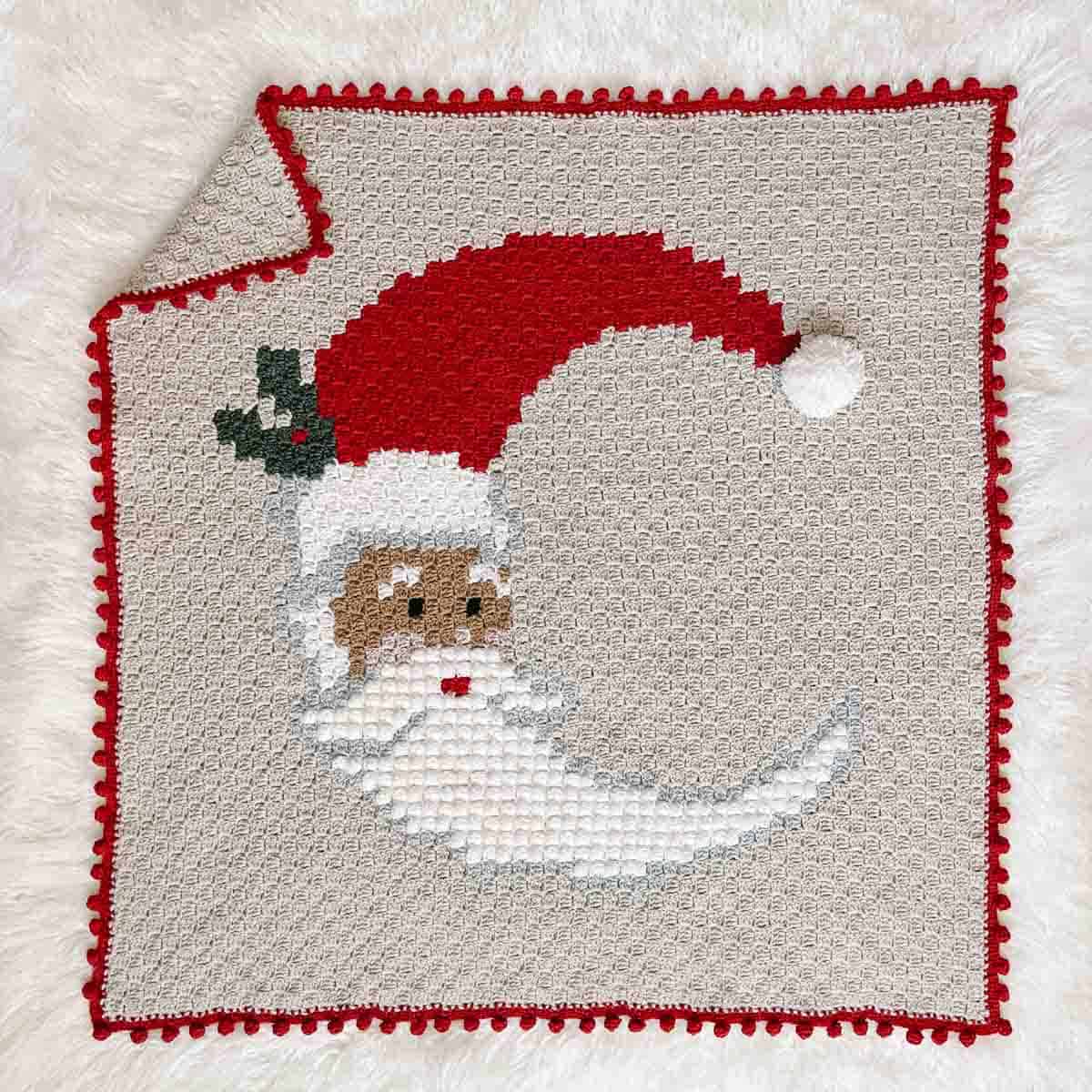 An overhead view of a c2c crochet blanket with a crescent-shaped Santa face.