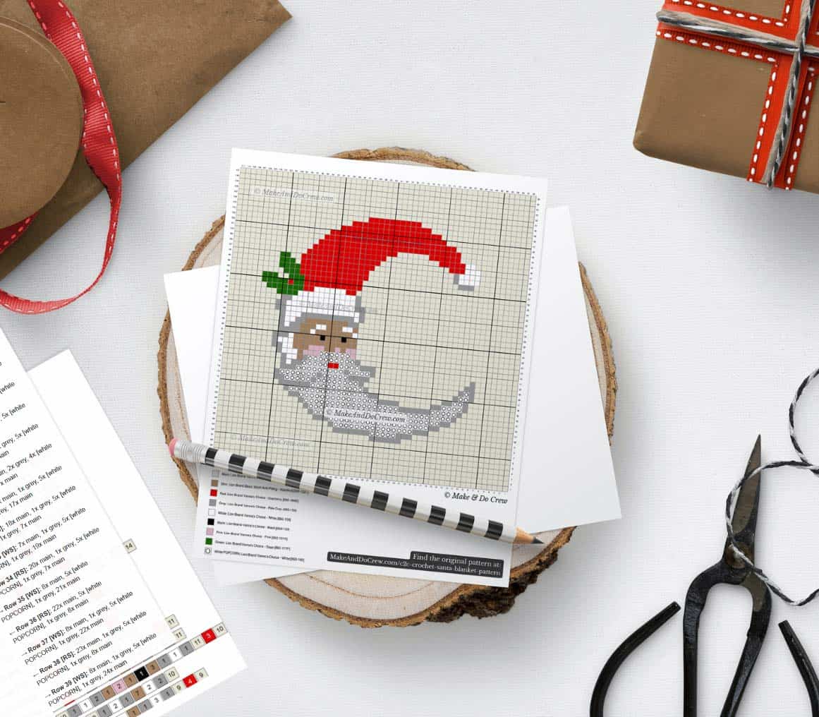 A flat lay Santa C2C crochet blanket pattern with a pencil, scissors, guide, and gift boxes around it on a white background. 