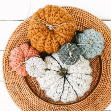 An overhead view of small, medium and large crochet pumpkins with jute tied around the stems. The pumpkins are setting on a wicker tray.