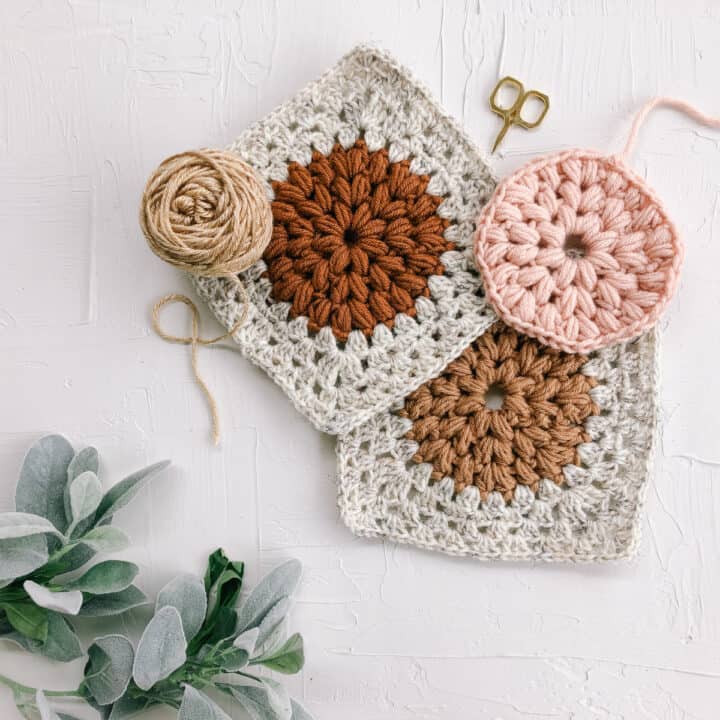 An overhead view of puff stitch granny squares stacked in a haphazard pile. The center of each square is a contrasting color puff stitch circle.