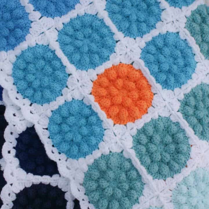 A blue bobble pop throw blanket with an orange detail.