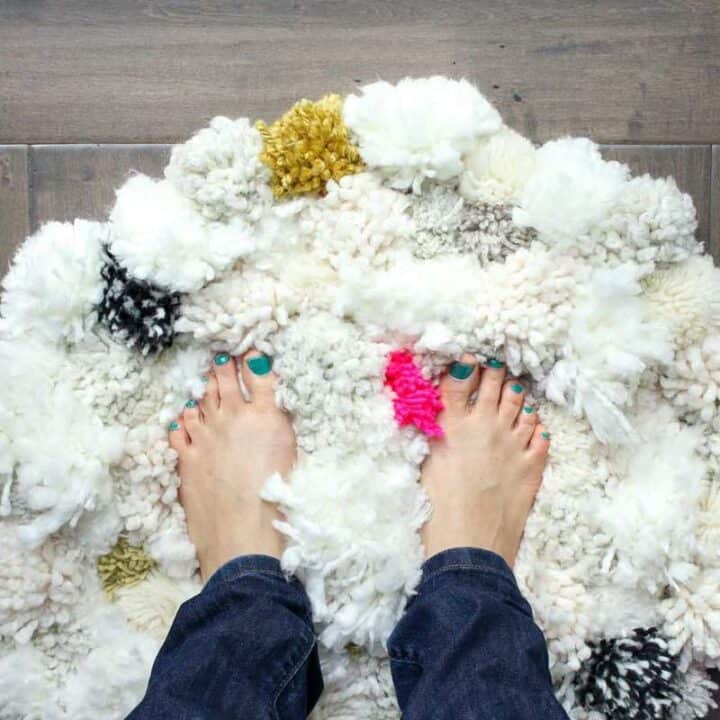 A woman's feet on a pom poms rug on the floor.