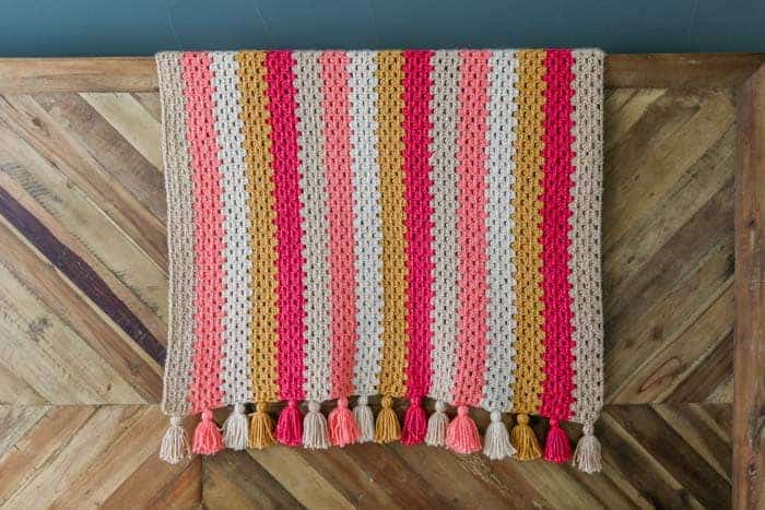 A modern granny stitch blanket draped on a wooden table.