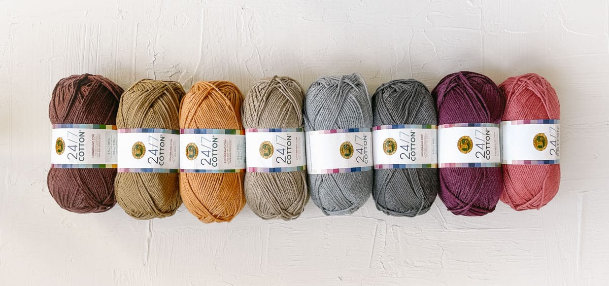 Many skeins of Lion Brand 24/7 Yarn in multiple colors lined up in a row.