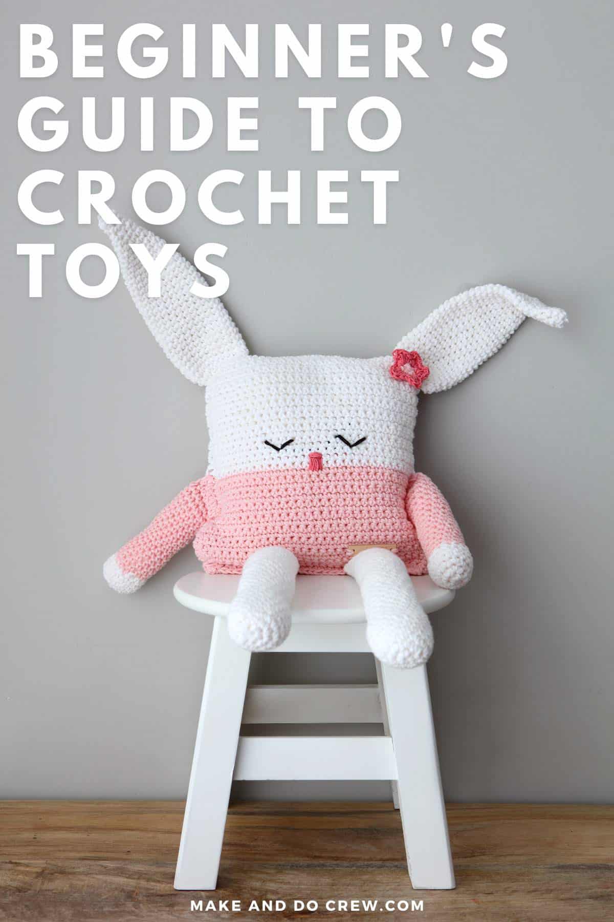 A crocheted bunny amigurumi doll is sitting on a white chair and leaning against a gray wall.