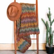 A crochet blanket hanging on a ladder.