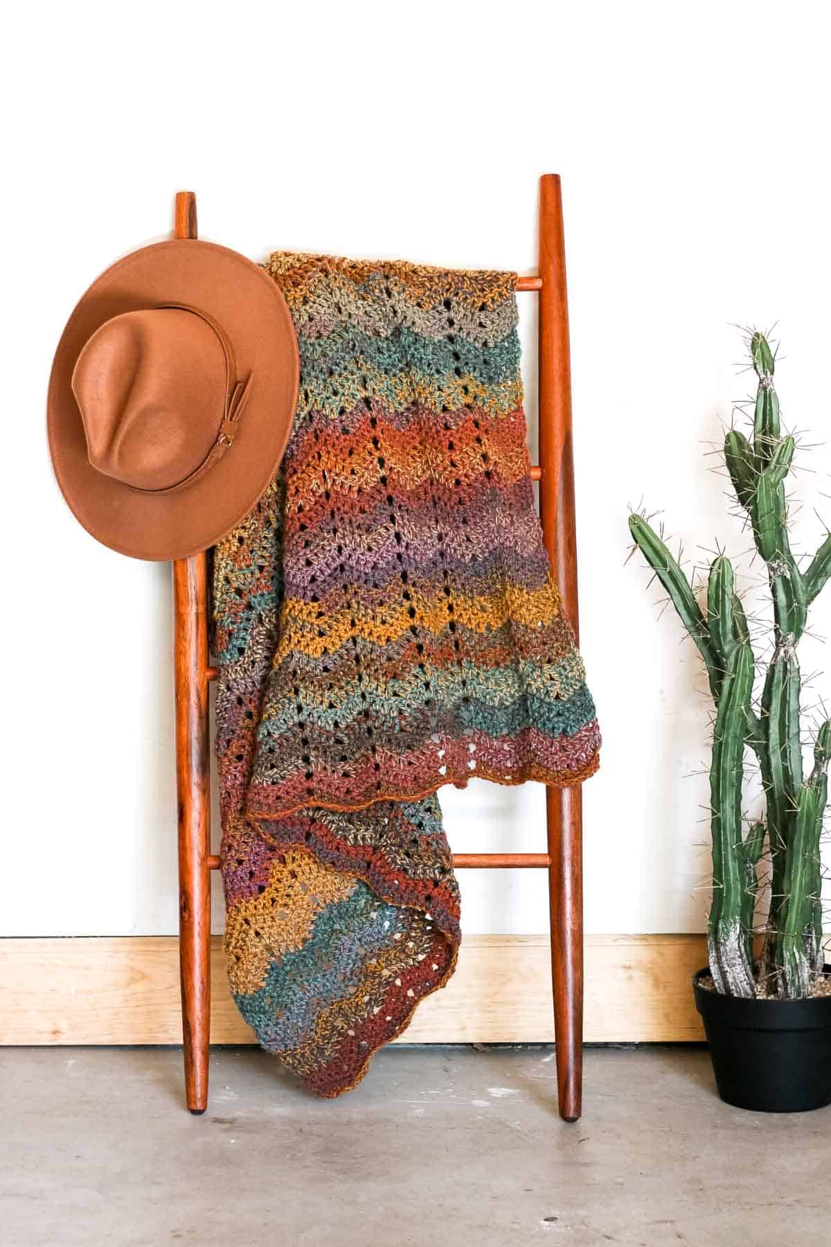 Hanging on a ladder is a crochet ripple blanket and a fedora hat.