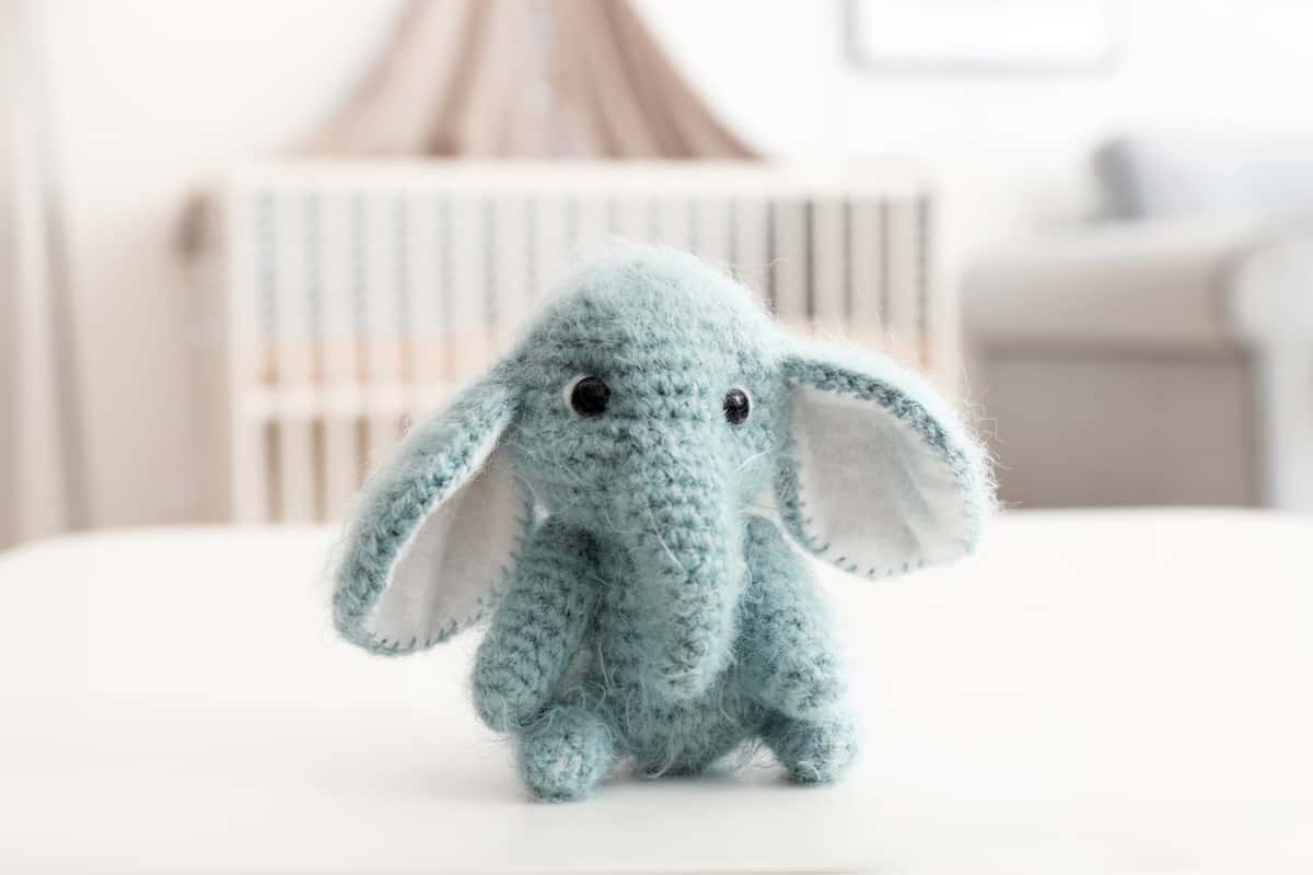 A bokeh shot of a crochet elephant amigurumi doll on top of a bed.