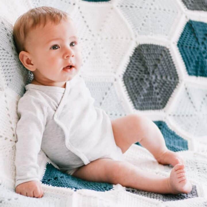 A baby sitting on a scrap yarn hexagon blanket.